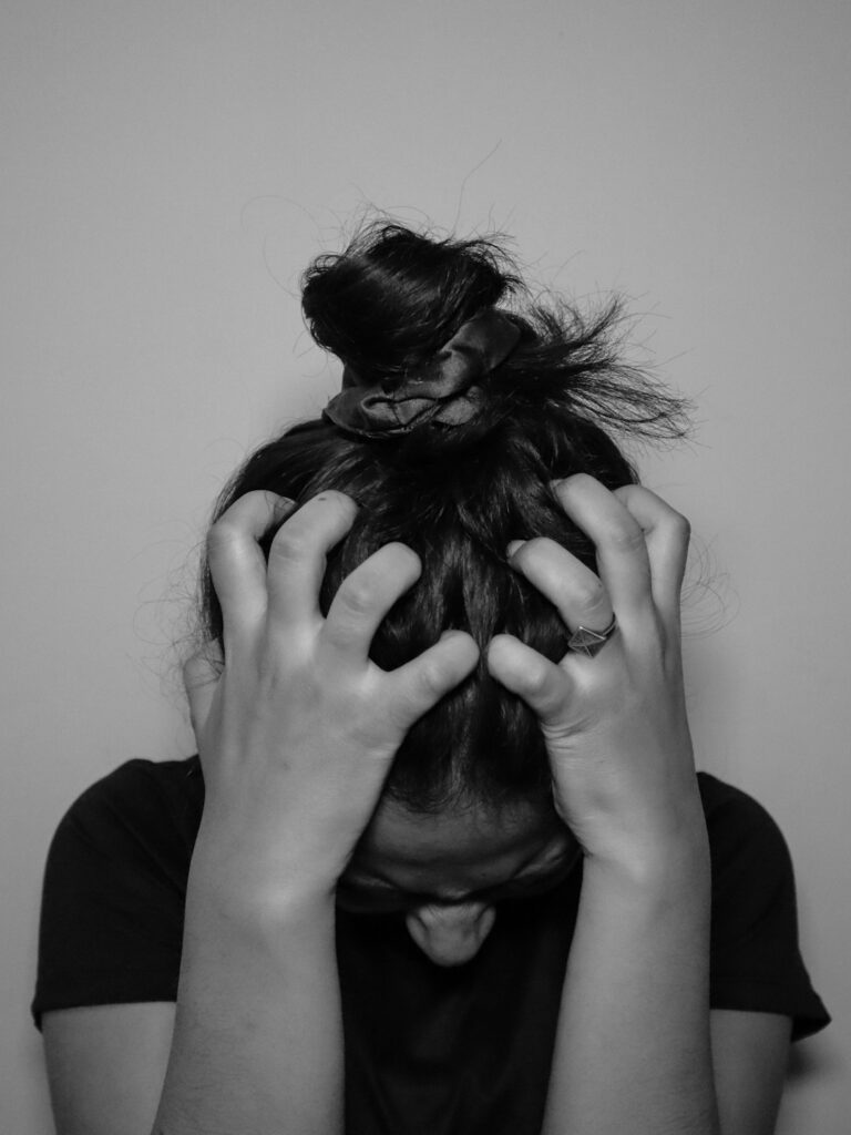 A young woman sits at a kitchen table looking worried, with her hands wrapped around a coffee mug.
