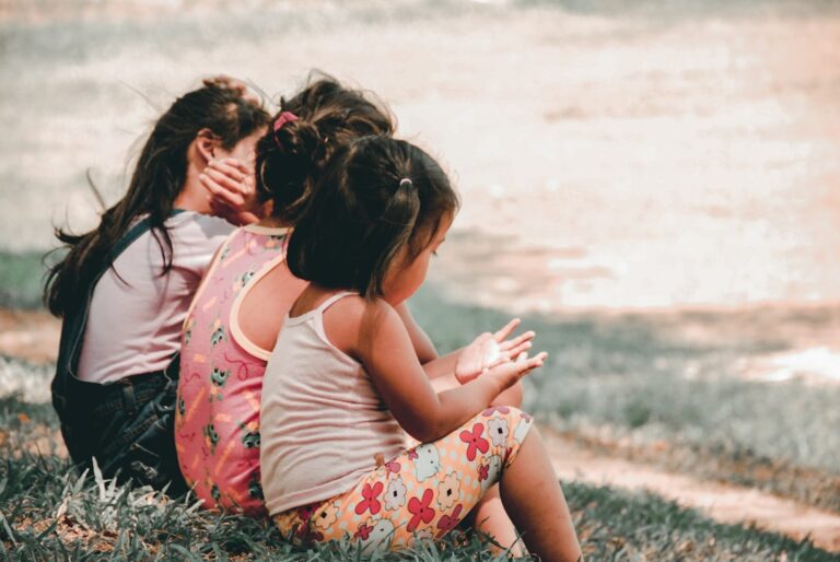 A parent sitting with a young child at a kitchen table, gently talking while the child draws with crayons.