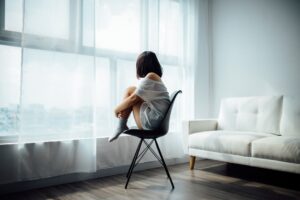 A person sits quietly by a window, looking outside on a gray day with a thoughtful expression.