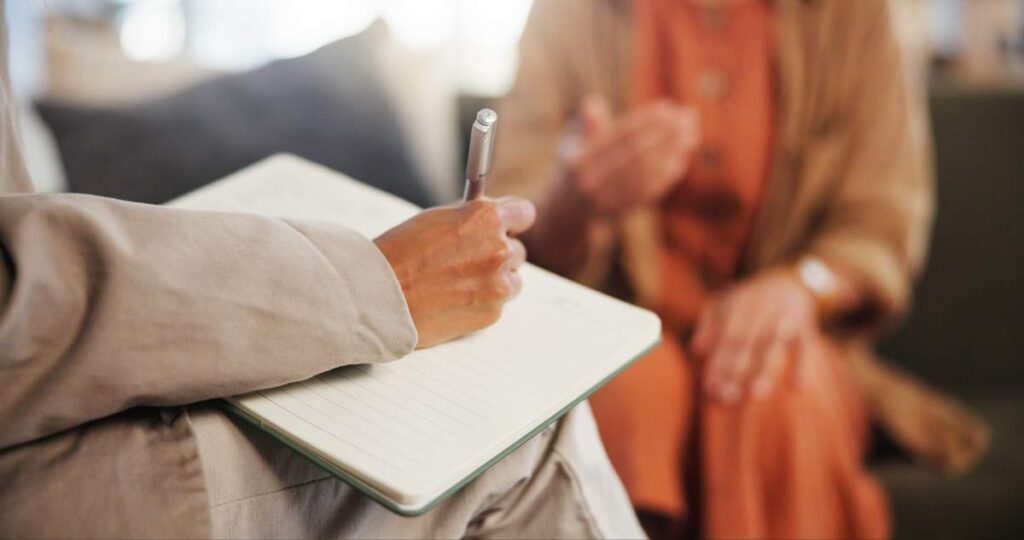 Person sitting quietly at a kitchen table, taking slow breaths beside a journal and warm drink.